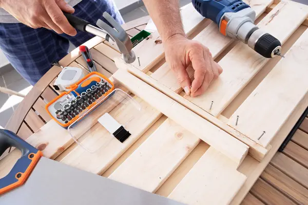 Person Repairing Wooden Furniture with Hammer and Drill on a Table