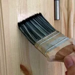 Hand applying wood repair marker to light pet scratches on wooden table leg