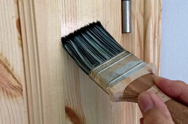 Hand applying wood repair marker to light pet scratches on wooden table leg